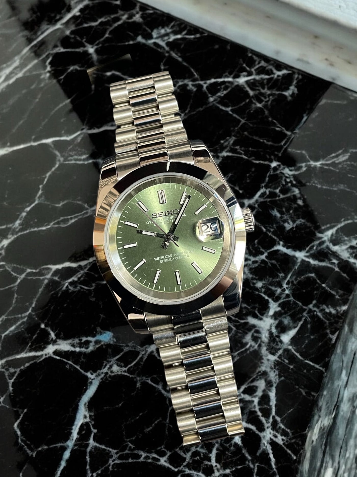Silver watch with a green face on a black marble surface