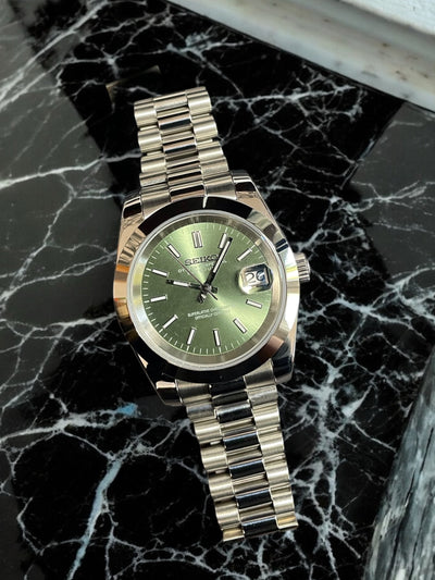 Silver watch with a green face on a black marble surface