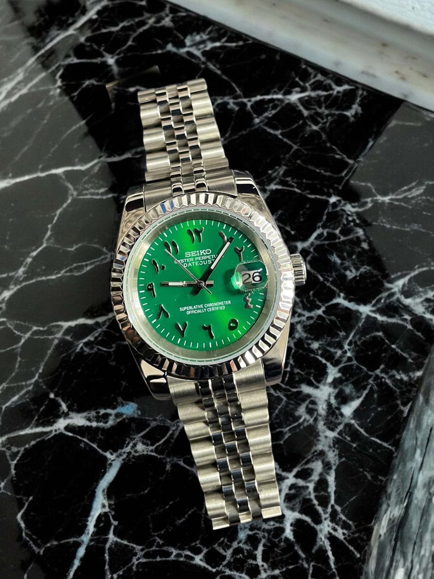 Silver watch with a green face on a black marble surface