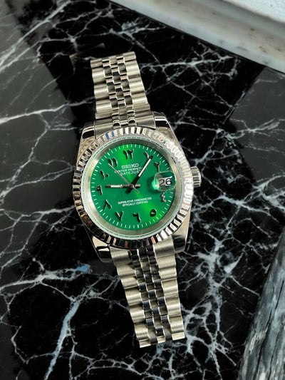 Silver watch with a green face on a black marble surface