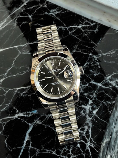 Silver watch with a black face on a black marble surface