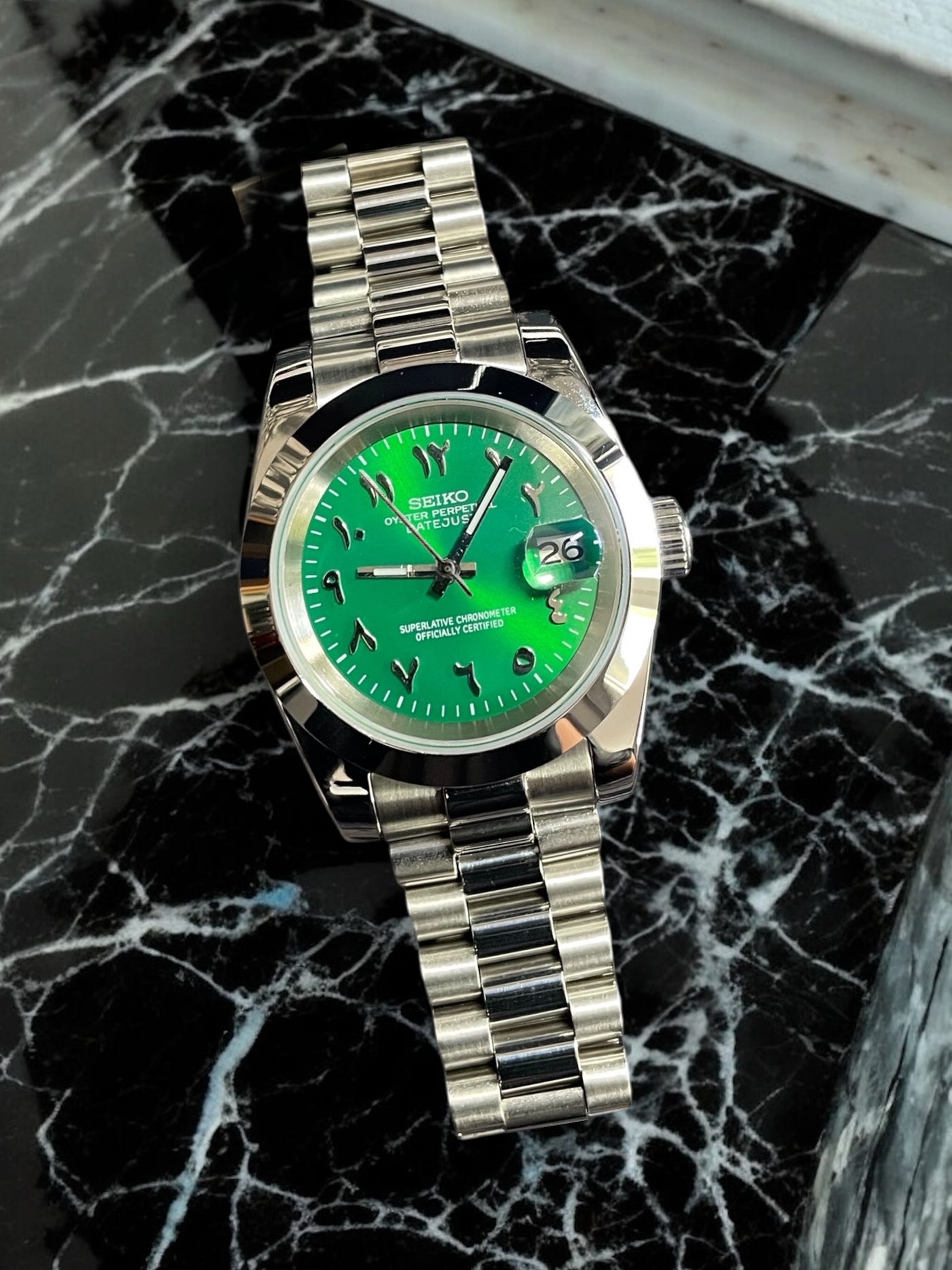 Silver watch with a green face on a black marble surface