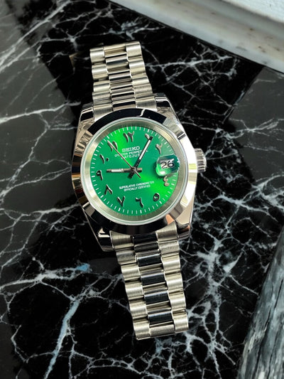 Silver watch with a green face on a black marble surface