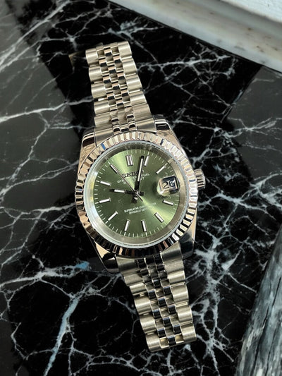 Silver watch with a green face on a black marble surface