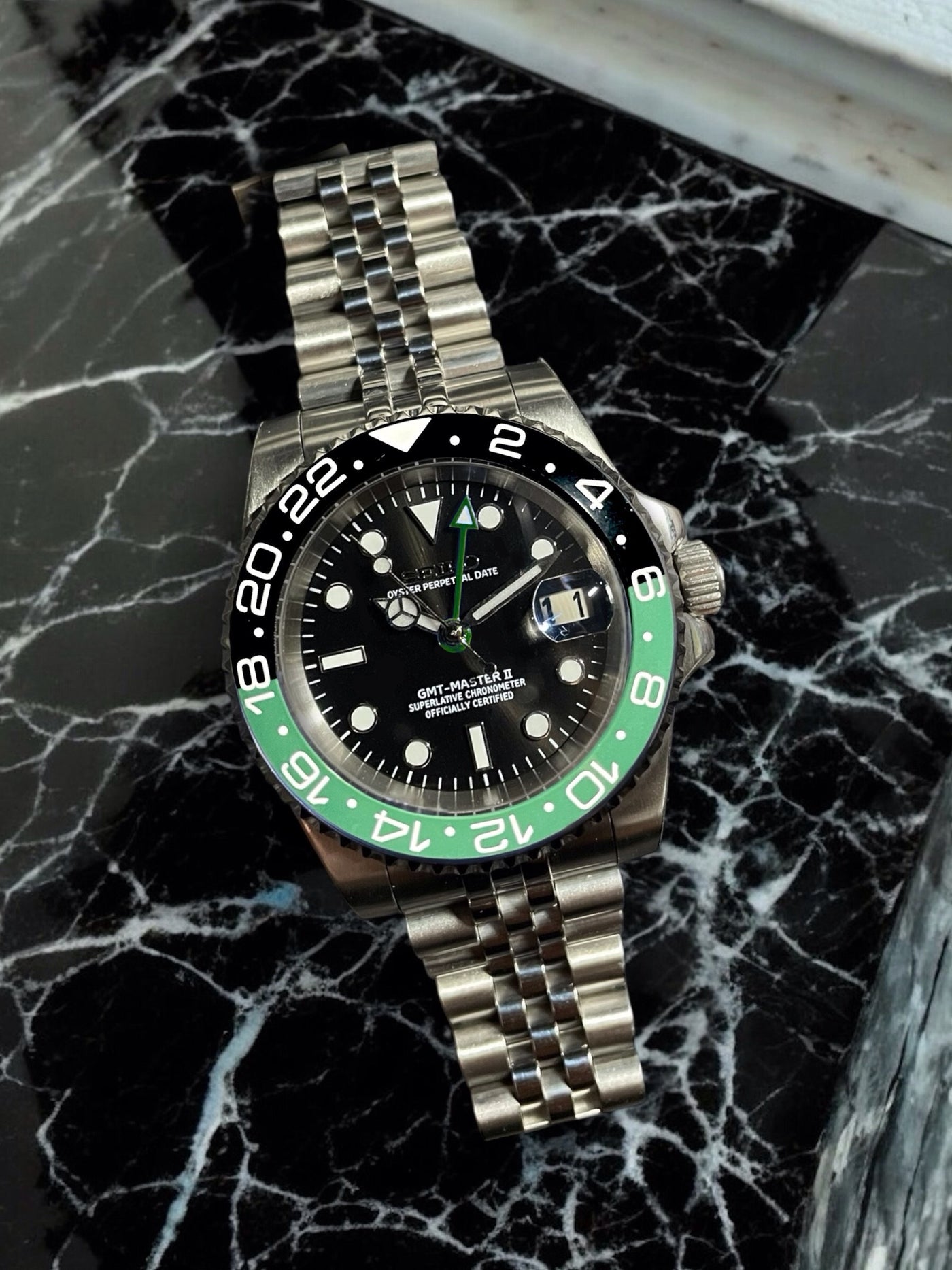 Silver watch with a black and green face on a marble surface
