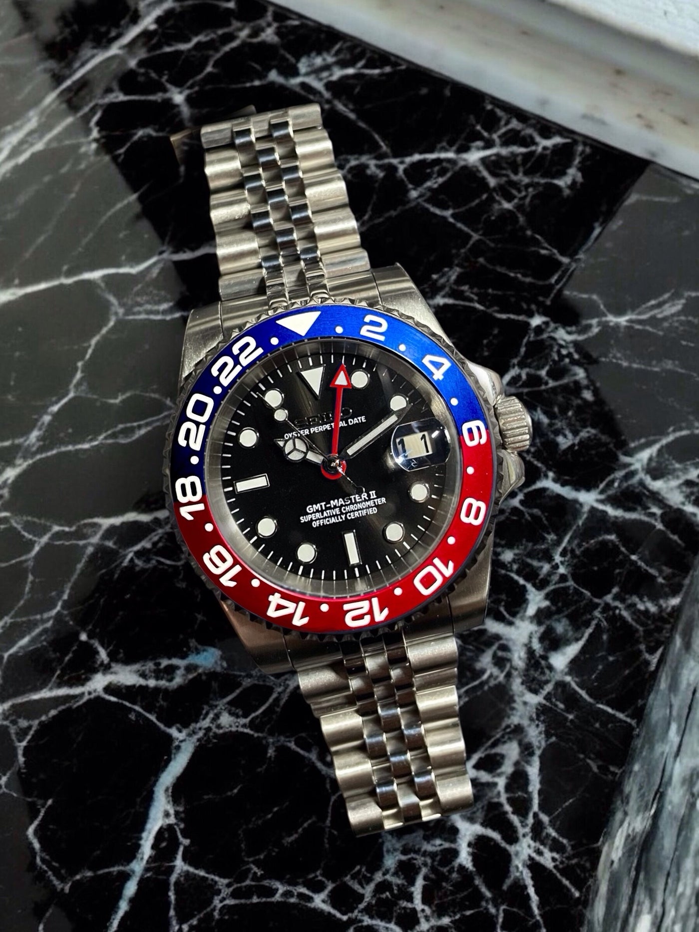 Watch with a distinctive red and blue bezel on a black marble surface