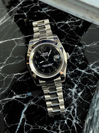 Silver Seiko watch with black face on a marble surface
