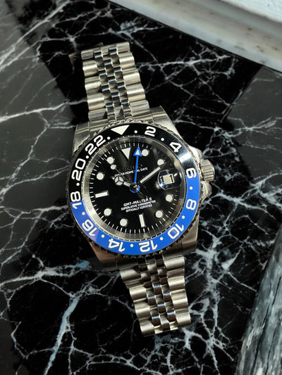 Silver watch with a black and blue face on a marble surface
