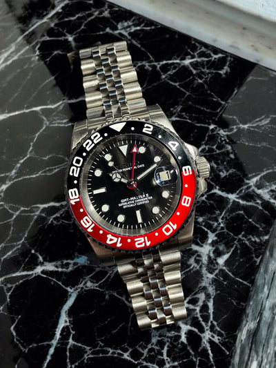 Watch with a silver bracelet and black and red face on a marble surface