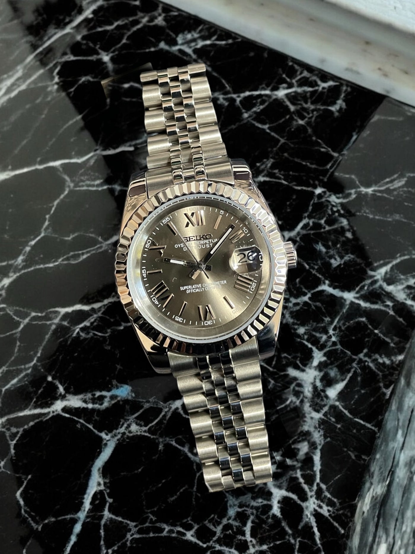 Silver watch with a dark face on a black marble surface
