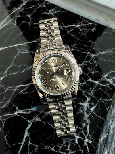 Silver watch with a dark face on a black marble surface