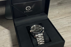 Silver watch in a black box with 'BC Watches' branding on a wooden surface